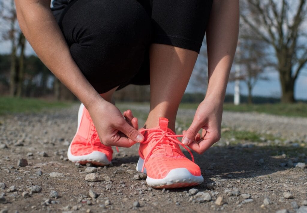 Joggerin sitzt in der Hocke und bindet sich die Sportschuhe zu